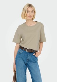 Beige kortærmet t-shirt med rund hals, parret med blå jeans. Outfittet har et brunt bælte med detaljer i sølvspænde.