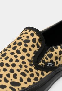 Chaussure slip-on Vans en toile à imprimé léopard beige et noir avec bordure noire autour de l'ouverture et de la semelle.