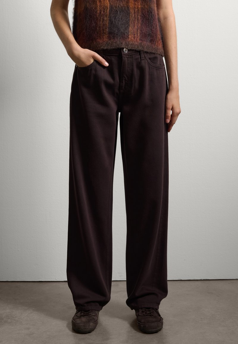 Pantaloni marroni scuri, dalla vestibilità ampia e con vita alta, dotati di tasche frontali e chiusura con bottone metallico. Realizzati in un morbido tessuto texturizzato.