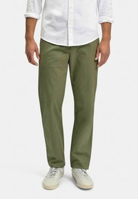 Olivgrön chinos i bomullsmix, rak passform, med sidofickor och en smidig yta, kombinerade med ljusa sneakers.