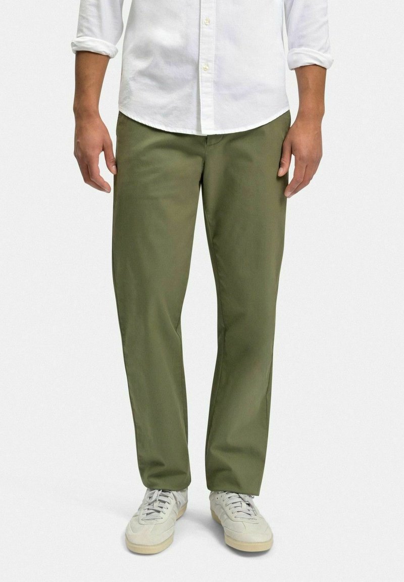 Olivgrön chinos i bomullsmix, rak passform, med sidofickor och en smidig yta, kombinerade med ljusa sneakers.