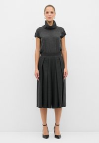 Grå cowl neck-top med korta ärmar, parat med en hög midja, plisserad midikjol. Svarta klackar med ankelsnöre fulländar outfiten.