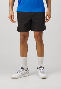 Sorte atletiske shorts, let stof, midt-lår længde. Parret med hvide sneakers og strømper i crew-længde. Simpel design.