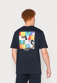 Laivastonsininen puuvillainen t-paita, jonka takana on värikäs grafiikka ja teksti "LOVE WINS", suorakaiteen muotoisella suunnittelulla ja blokkimaisilla väreillä.