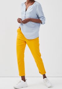 Light blue, button-up shirt with rolled sleeves; paired with bright yellow, cropped pants; white sneakers complete the outfit.