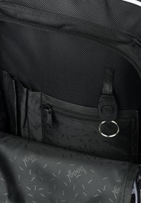 L'interno dello zaino nero presenta un tessuto testurizzato, una tasca con zip, numerosi scomparti e una fodera decorata con piccoli accenti ripetuti.