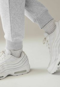 Weiße Sportsneaker mit Mesh- und Lederdetails, getragen mit hellgrauen gerippten Socken. Graue Jogginghosen mit elastischen Bündchen sind sichtbar.