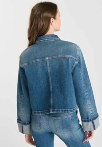 Jeansjacka i ljusblå färg med avslappnad passform och kontrasterande ärmslut. Märkbar sömnad längs sömmarna och knapppdetalj på kragen.