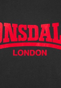 Fekete pamut póló, amelynek élénk piros betűi azt írják, hogy "Lonsdale" és "London", egy ívelt aláhúzással alatta.