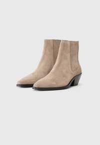Stivali ankle in suede beige con punta affilata, pannelli laterali testurizzati e tacco basso e affusolato. Finitura liscia con dettagli minimi.