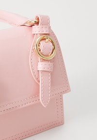 Pink patent leather handbag with a structured design, featuring gold hardware and a stitched accent along the edges.