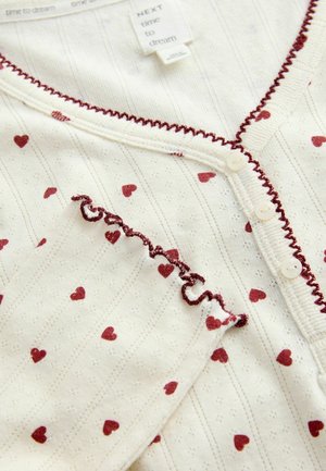 Long-sleeve, lightweight cream top with maroon heart patterns and textured stripes. It features button closures and ruffled edges along the neckline.