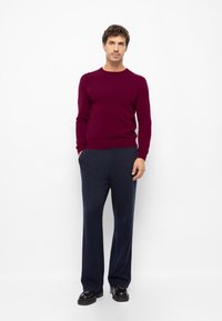 Bordeauxrode gebreide trui met lange mouwen, gecombineerd met loszittende marineblauwe broek en zwarte schoenen. Eenvoudig ontwerp, zachte textuur en comfortabele pasvorm.