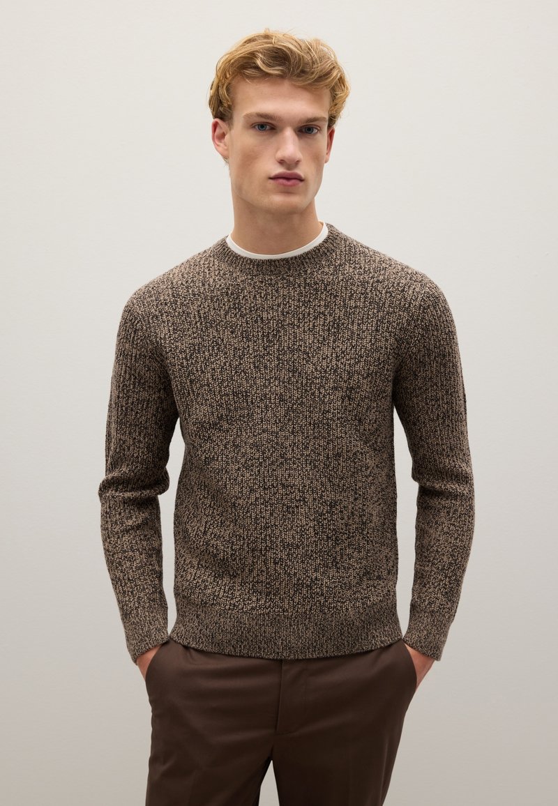 Maglione a maglia marrone con texture, collo a giro e maniche lunghe, caratterizzato da un orlo a coste, indossato su una camicia bianca.