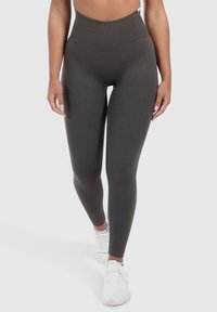 High-waisted harmaan legginsit, jotka on valmistettu joustavasta ribbikankaasta, jossa on tiukka siluetti ja sileä pinta, yhdistettynä valkoisiin urheilukenkiin.