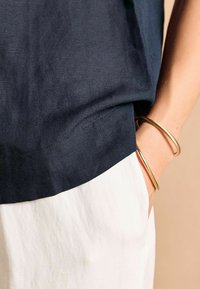 Tumed linane topp valge puuvillase alumise äärisega, millel on sile tekstuur ja kuldne käevõru randmel.