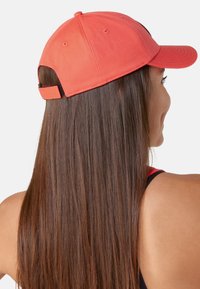 Cappellino da baseball rosso con visiera curva, cinturino regolabile sul retro e dettagli di cucitura visibili. Tessuto liscio.