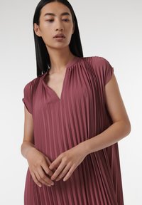 Robe plissée prune avec décolleté en V et manches courtes, fabriquée en tissu doux. Présente des plis verticaux et une silhouette décontractée.