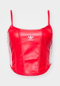 Raudonas trumpas marškinėlis, pagamintas iš blizgaus sintetinio pluošto, su baltais šoninių juostelių ir Adidas logotipu centre. Reguliuojamos špagetės petnešėlės.