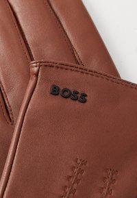 Brown leather glove featuring subtle stitching details and a black "BOSS" logo accent. Smooth texture with a fitted design.