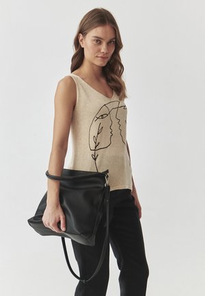 Top beige senza maniche con disegni in linea nera di volti e foglie, abbinato a una grande borsa in pelle nera con zip e tracolla.