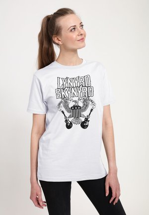 Bílý bavlněný tričko s černým grafickým designem orla, kytar a textem "LYNYRD SKYNYRD", s krátkým rukávem a volným střihem.