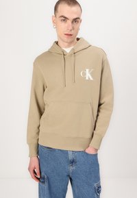 Bežinis džemperis su priekinė kišene, su raišteliu reguliuojama kapuca ir baltu "CK" logotipu. Minkšta medvilninė medžiaga ir gumuoti rankovių bei apačios kraštai.