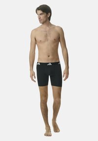 Boxer da uomo neri con design aderente, dotati di una ampia cintura elastica con il logo Adidas bianco e tre strisce sul davanti.