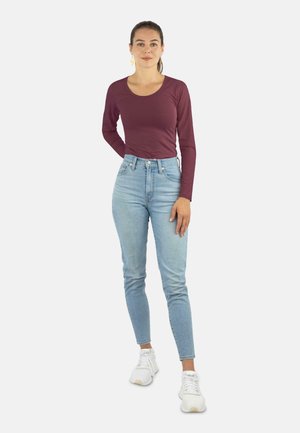 Langärmliges burgunderfarbenes Oberteil, kombiniert mit hochgeschnittenen hellblauen Jeans und weißen Turnschuhen. Das Oberteil hat einen runden Halsausschnitt und einen schlanken Schnitt.