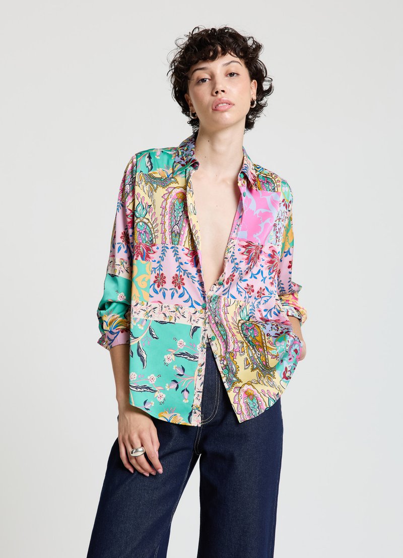 Chemise imprimée colorée avec un mélange de motifs turquoise, rose et jaune, à coupe décontractée et manches retroussées. Texture de tissu à motifs.