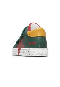 Sneaker basse avec tige en cuir vert et rouge, boucle de talon jaune, semelle blanche tachetée et texte rouge "@74" sur le côté.