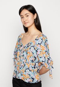 Blusa floral feita de tecido leve, com fundo azul-marinho e flores laranja e aqua, decote em V e mangas bufantes.