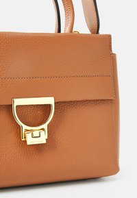 Sac à main en cuir brun avec une finition texturée, doté d'une fermeture en métal doré et de poignées supérieures. Design minimaliste avec une forme structurée.