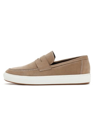 Mocasín de ante beige con un diseño slip-on, suela de goma blanca, detalle de costura y una textura suave. Cuenta con una banda superior prominente en la parte superior.