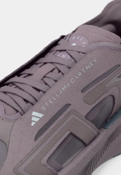 Μωβ αθλητικό παπούτσι με πάνελ από δίχτυ, υφή στην επιφάνεια, κορδόνια σε τόνο και λογότυπο "STELLA MCCARTNEY". Διακριτικές γεωμετρικές πινελιές σχεδίου.