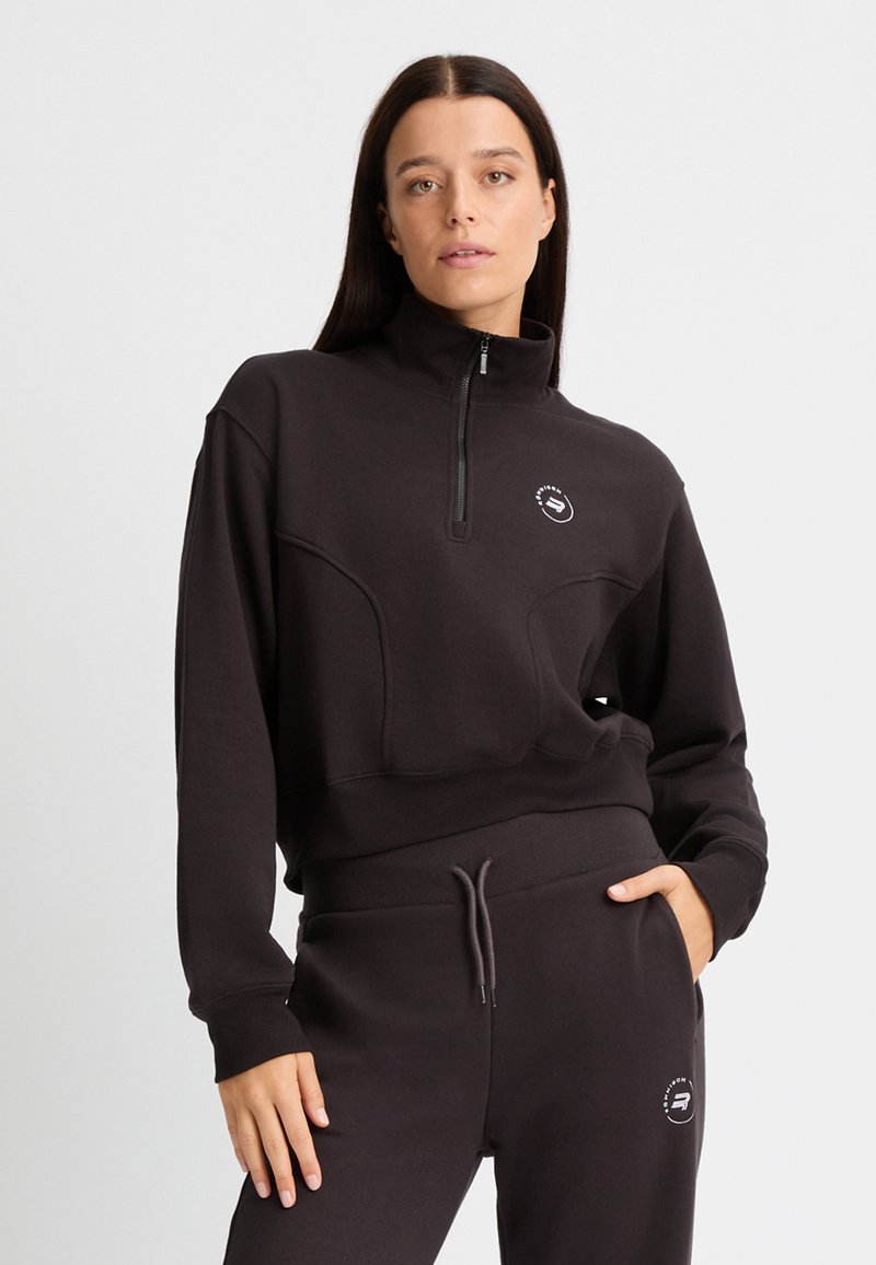 Pullover nero con zip e colletto alto, con cuciture tonali, presenta un logo sul petto e pannelli testurizzati, abbinato a pantaloni della tuta coordinati.