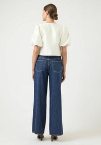 Bílý krátký top s nafouknutými rameny a krátkými rukávy, zkombinovaný s džínami s vysokým pasem a širokými nohavicemi modré barvy. Hladká látka s volným střihem.