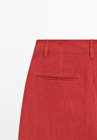 Rode stoffen broek die het bovenste deel van de rug toont met riemlussen en een enkele paspelzak aan de rechterkant.