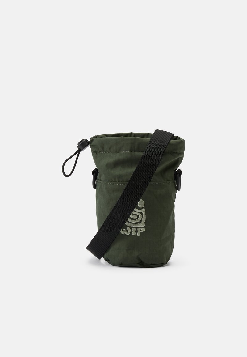 Saco de nylon verde com um topo de cordão, alça preta ajustável e logótipo impresso na parte da frente. Textura suave, formato cilíndrico.