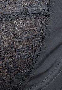 Μαύρο δαντέλα με λουλούδια δίπλα σε λείο, συμπαγές μαύρο ύφασμα με λεπτομερή ραφή.