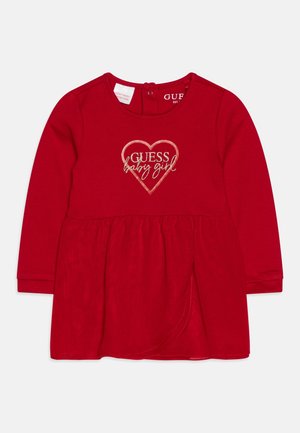 Rotes Baby-Kleid mit langen Ärmeln und gerafftem Rock, vorne mit einem gold bestickten Herzdesign "GUESS baby girl". Weiche Stofftextur.