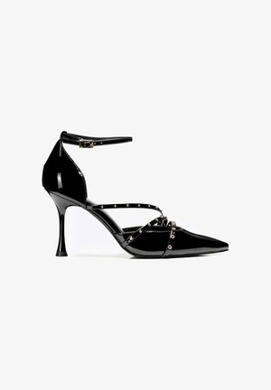 Schwarzer Lackleder-High-Heel-Schuh mit spitzem Zeh, Knöchelriemen und metallischen Nieten entlang der Riemen. Verfügt über einen schmalen Stiletto-Absatz.