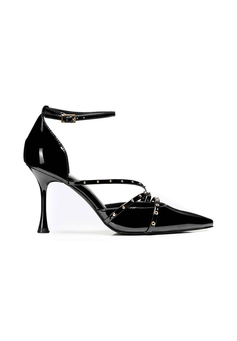 Scarpa con tacco alto in pelle sintetica nera, punta affusolata, cinturino alla caviglia e borchie metalliche lungo i cinturini. Presenta un tacco stiletto sottile.