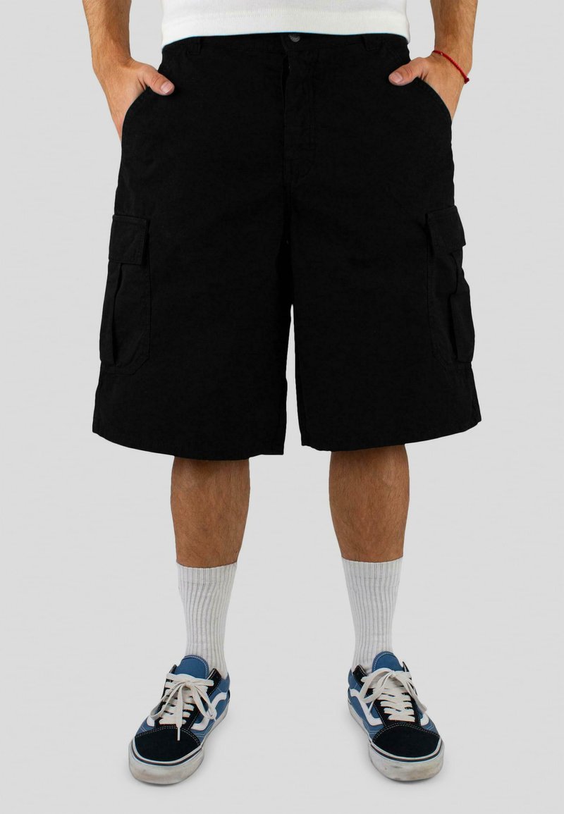 Pantalones cortos de carga negros con bolsillos laterales, cierre de botón y corte ajustado, combinados con calcetines blancos y zapatillas con detalles en azul.