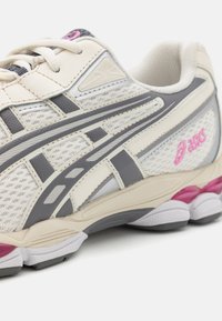 Skriešanas apavi ar krēmīgu acs augšdaļu, pelēkiem akcentiem, rozā logotipu, ar mīkstu balto zoli, kurai ir pelēki un violeti akcenti, uzsverot ventilējamu dizainu.