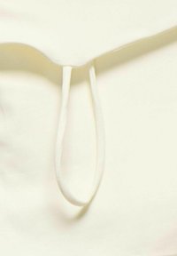 Tissu couleur crème avec une texture lisse, présentant un col rond et un détail en boucle à l'épaule. Design simple et minimaliste.