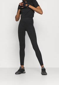 Svarta träningsleggings med hög midja, slät yta och nätdetaljer längs sidorna, kombinerade med en svart t-shirt med kort ärm.