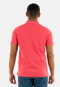 Polo shirt corail avec un col classique, des manches courtes et une subtile accent blanche au col. Associé à un jean bleu.