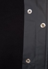 Panneau de tissu noir et gris avec des boutons en métal argenté. La surface texturée est lisse du côté gris et douce du côté noir.