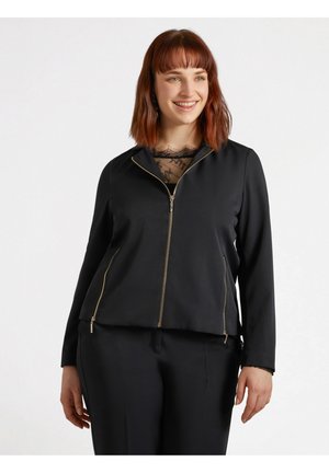 Black zip-up jacket with gold hardware; features long sleeves, a high collar, and a relaxed fit. Worn over a lace top.